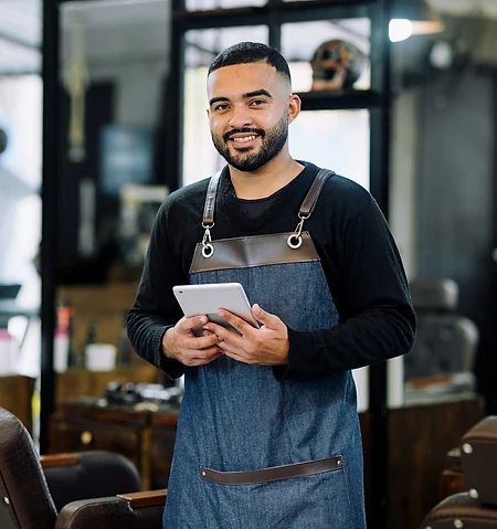 A barber smiling in his shop, holding a tablet