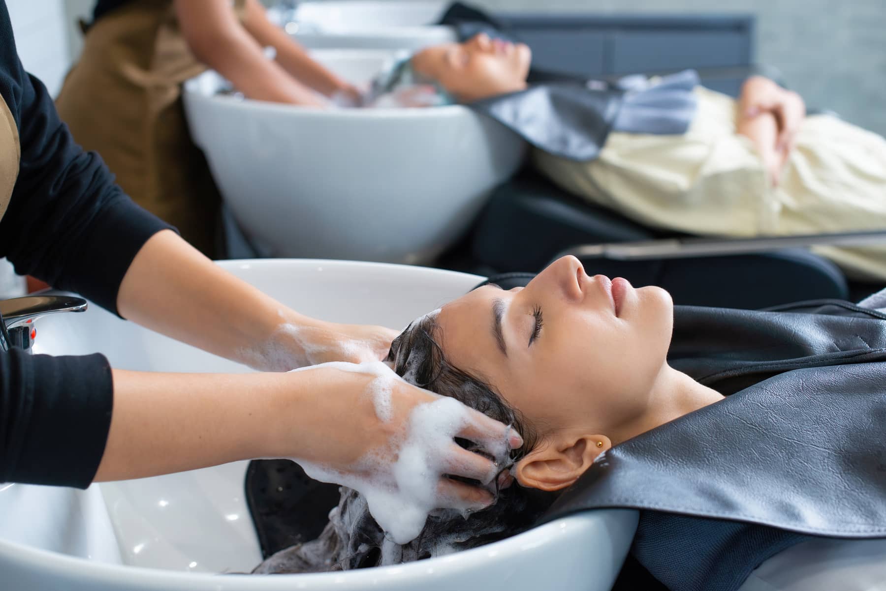 Stylist washing a relaxed client's hair at a salon backwash basin.